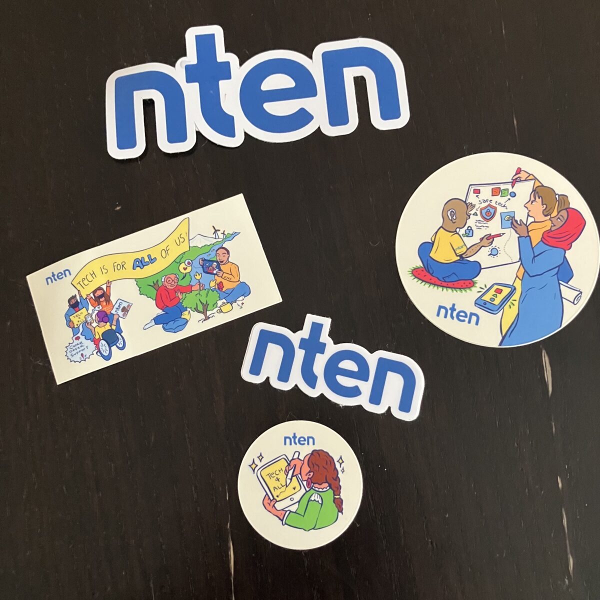 Five stickers. Two are blue and white with the letters nten. Two are circular and picture people using technoloyg. One is rectangular and shows people using technology with the caption "technology is for everyone."